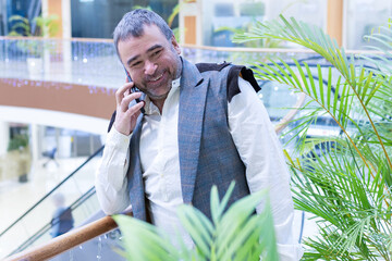 Emotional businessman talking on smartphone in modern office with green plants. High quality photo