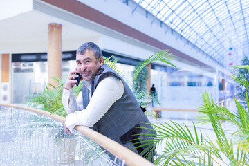 Emotional businessman talking on smartphone in modern office with green plants. High quality photo