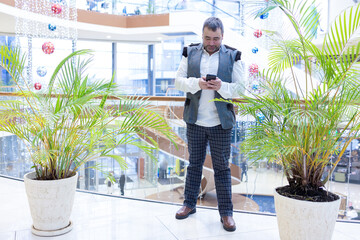 Emotional businessman talking on smartphone in modern office with green plants. High quality photo