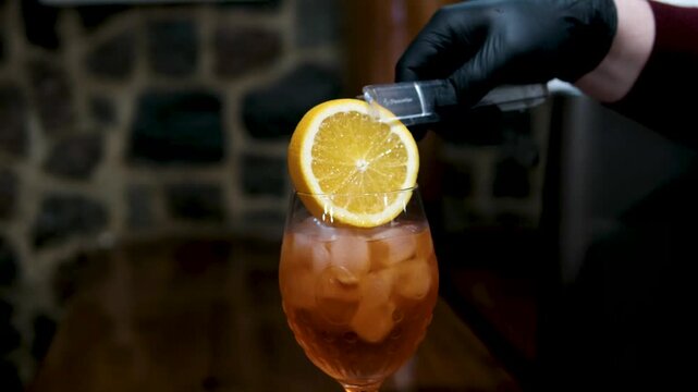 add a slice of orange Aperol Person preparing summer refreshing aperol spritz cocktail party, bartender adding slices of orange ice cubes and aperol, fizzy alcohol beverage preparation. 