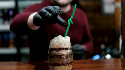 A bartender sticks a green plastic straw into a chocolate-coffee drink with cream. High quality 4k footage