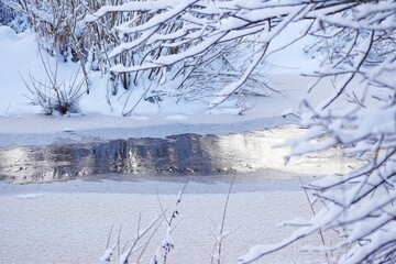 Partially frozen river with snow-covered branches in winter
