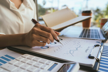 A person reviews financial charts while using a calculator and laptop on a desk, focusing on data analysis and business planning.