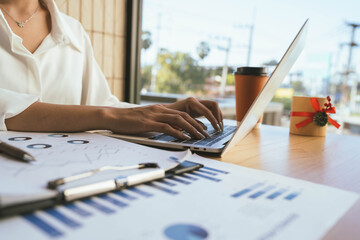 A person reviews financial charts while using a calculator and laptop on a desk, focusing on data analysis and business planning.