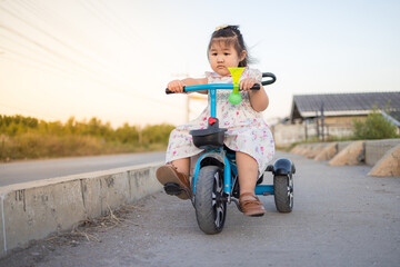 A cute little Asian girl is having fun riding a tricycle in the evening,Japanese girl riding on the tricycle (2 years old) and cherry blossoms,Children's Day.