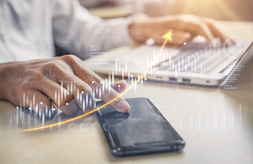 A businessman analyzes financial data trends on a laptop while a smartphone lies nearby in a modern...