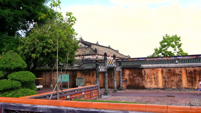 Ochre wall of Hue Imperial City with traditional tiled gate and lush green trees.