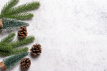 Minimalist Christmas background with fir branches, pinecones, and small decorative trees on white rustic cement surface. Perfect for holiday greetings, winter promotions, and seasonal templates.