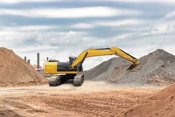 Obraz premium Excavator works on a construction site, moving piles of gravel around while clouds linger in the sky, indicating a busy work environment