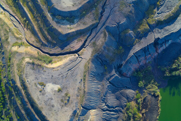 Top-down drone shot showing deep ravines cut through geological terraces and a pool of vivid green...