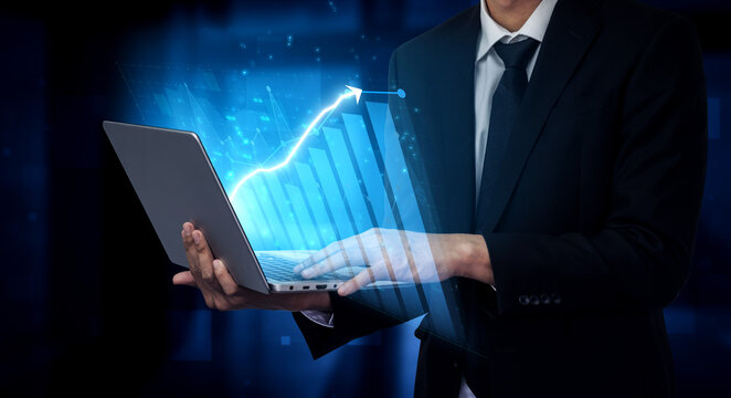 A businessman stands in a professional suit while holding a laptop that visually represents growth data through digital graphics, embodying modern business efficiency. Impute