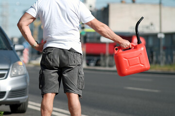 Stranded man signals for help, Driver in white shirt and grey shorts calls for assistance, Man with red fuel container flags passing vehicles while stranded near parked car