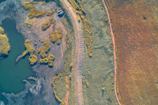 Abstract drone view showing a dirt path dividing a dark, contaminated industrial waste lake from a textured field. The sharp contrast highlights the ecological crisis and human impact on nature