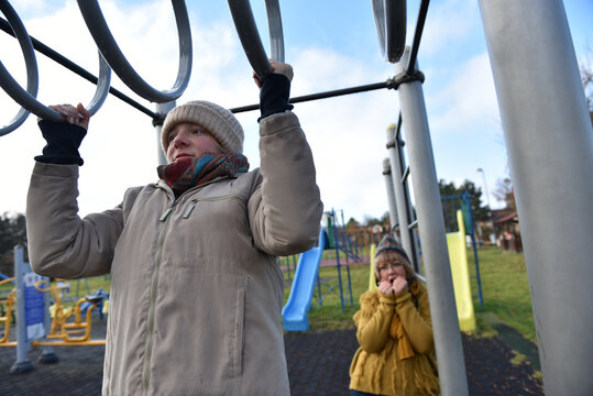 Teenager daughter and mother using gymnastic rings in outdoor gym park - Powered by Adobe