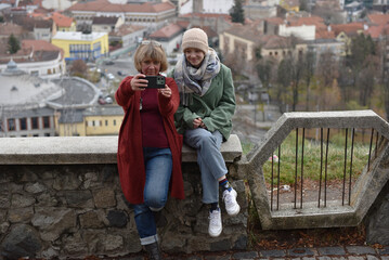 Fototapeta premium Mother and young adult teenager daughter taking a selfie outdoors with a city view