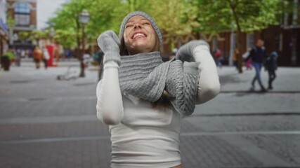 Woman laughing with mouth open on street, wearing knit hat and scarf and mittens, leaning forward toward camera; joy. - Powered by Adobe