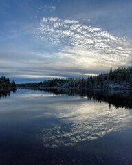 Calm lake reflecting evening clouds and forest shoreline under soft fading blue light