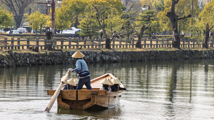 Traditional Japanese wooden sculling oar boat and with tourist wearing kasa hats along canal of Himeji castle in Himeji, Hyogo prefecture in Japan