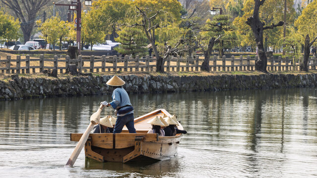 Traditional Japanese wooden sculling oar boat and with tourist wearing kasa hats along canal of Himeji castle in Himeji, Hyogo prefecture in Japan