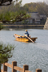 Traditional Japanese wooden sculling oar boat and with tourist wearing kasa hats along canal of Himeji castle in Himeji, Hyogo prefecture in Japan