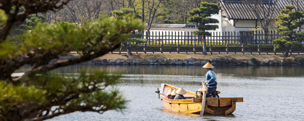 Traditional Japanese wooden sculling oar boat and with tourist wearing kasa hats along canal of Himeji castle in Himeji, Hyogo prefecture in Japan