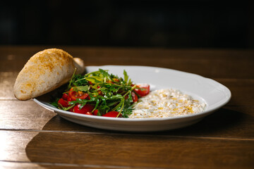 Healthy lunch plate with arugula salad, cherry tomatoes, creamy cheese dip and bread roll.
