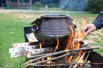 Person Cooking in Traditional Pot Over Open Fire Outdoors