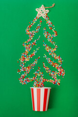 Multicolored sugar stars in the shape of a Christmas tree are scattered across a green background. A paper cup is also placed on the green background. Viewed from above, flat lay
