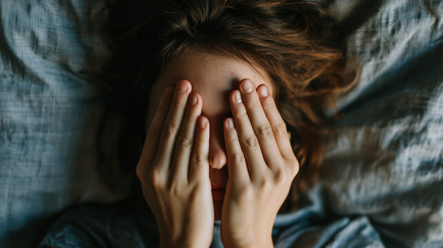 A woman lying in bed with her hands covering her eyes, having one of those nights where she can't sleep and is suffering from intense pain due to a migraine. Ai generated