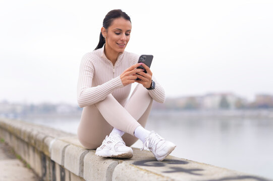 Woman smiling and checking phone outdoors near river