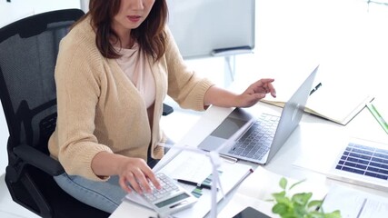 Asian adult woman calculating business finance laptop modern office sustainability renewable energy solutions project planning investment green economy - Powered by Adobe