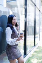 Fototapeta premium Happy businesswoman making phone call holding coffee outside