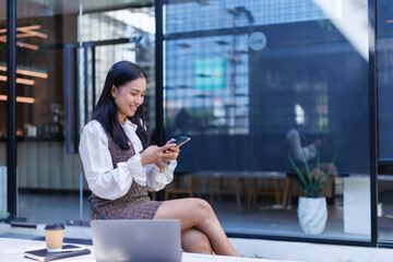 Woman smiling using smartphone outdoors in modern urban setting