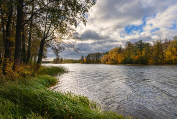 Autumn landscape with river, trees, and dynamic clouds