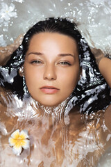 Relaxed Woman Washing Hair In Clear Water With Flower And Glowing Skin