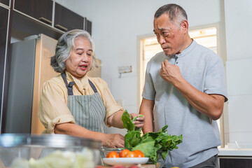 Asian senior couple preparing fresh vegetables in home kitchen, Elderly couple cooking healthy meal together at home, Senior lifestyle with couple washing and cutting vegetables in kitchen