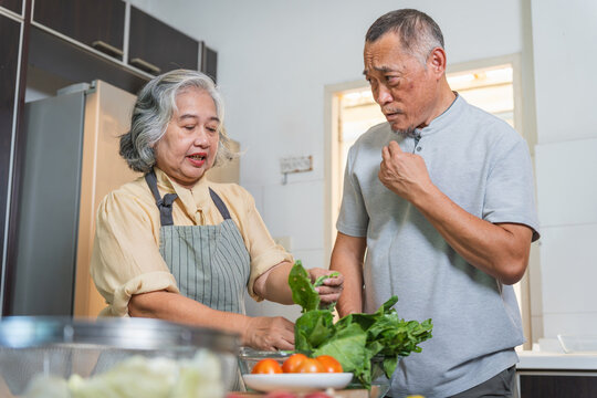 Asian senior couple preparing fresh vegetables in home kitchen, Elderly couple cooking healthy meal together at home, Senior lifestyle with couple washing and cutting vegetables in kitchen - Powered by Adobe