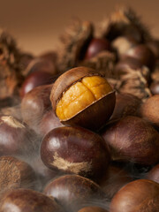 Freshly roasted chestnut with cracked shell emitting steam on a pile of nuts dark moody concept
