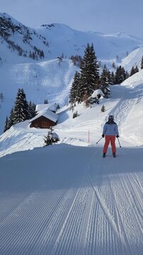 Woman skiing groomed alpine track past rustic hut in Stuben Arlberg Austria under sunny sky ideal for winter tourism ads.