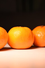 Vertical photo: one tangerine clearly visible in the center, side ones partially visible, dark background, close-up
