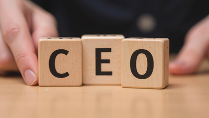 Wooden blocks spelling CEO, symbolizing leadership and business success, with hands gently placing them on table