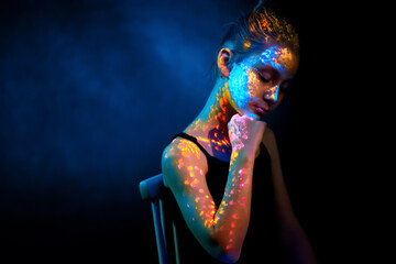 Portrait of a woman with neon UV paints on her face and body. Concept of bright art makeup, fluorescent colors, modern art, and creative visual aesthetics.