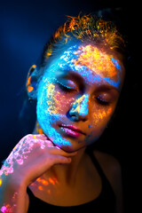 Portrait of a woman with neon UV paints on her face and body. Concept of bright art makeup, fluorescent colors, modern art, and creative visual aesthetics.