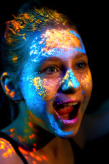 Portrait of a woman with neon UV paints on her face and body. Concept of bright art makeup, fluorescent colors, modern art, and creative visual aesthetics.