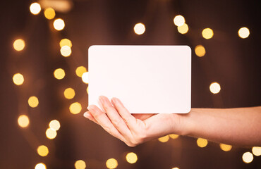 Obraz premium white sheet of paper copy space in a woman's hand against the background of New Year's bokeh