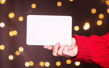 Obraz premium white sheet of paper copy space in a woman's hand against the background of New Year's bokeh