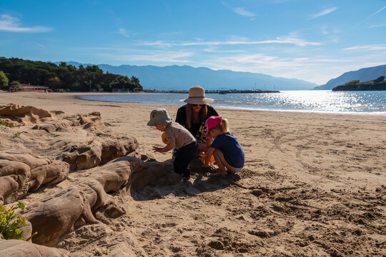 Mother and two children playing with sand on Paradise beach in Lopar, Rab island, Croatia, building sandcastles near rocky formations during a sunny family vacation on the beautiful Adriatic coast.
