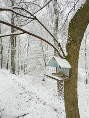 birdhouse feeder on tree branches, it is snowing heavily in the park, large flakes of snow are slowly falling on tree branches