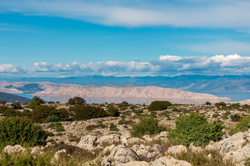 A scenic landscape view featuring the rocky terrain and dry stone walls of Kamenjak mountain overlooking the blue Adriatic Sea and the majestic Velebit mountain range in the background in Croatia.
