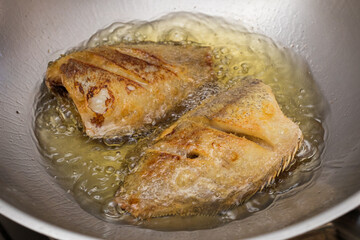 Close-up of Thai-style snakeskin gourami being fried in a pan with boiling oil, showing crispy golden texture.